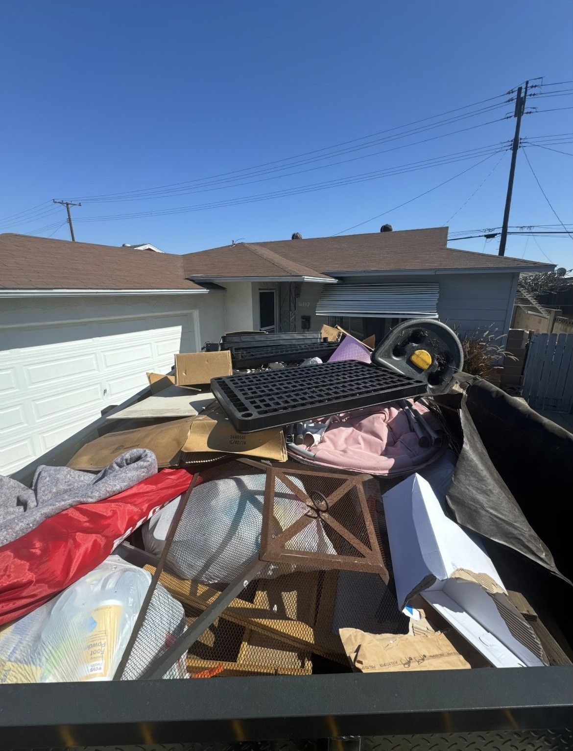 A dumpster overflowing with household junk under a blue sky, with houses in the background.
