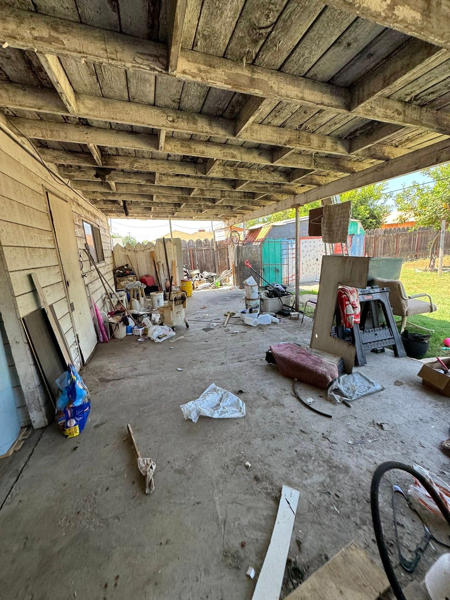 Covered outdoor space cluttered with debris, under a weathered wooden ceiling.