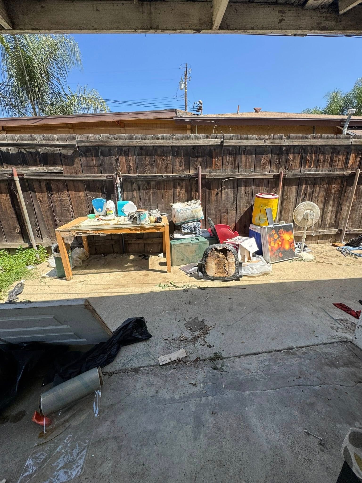 Backyard with debris: table, trash, fence, sky, and patio.