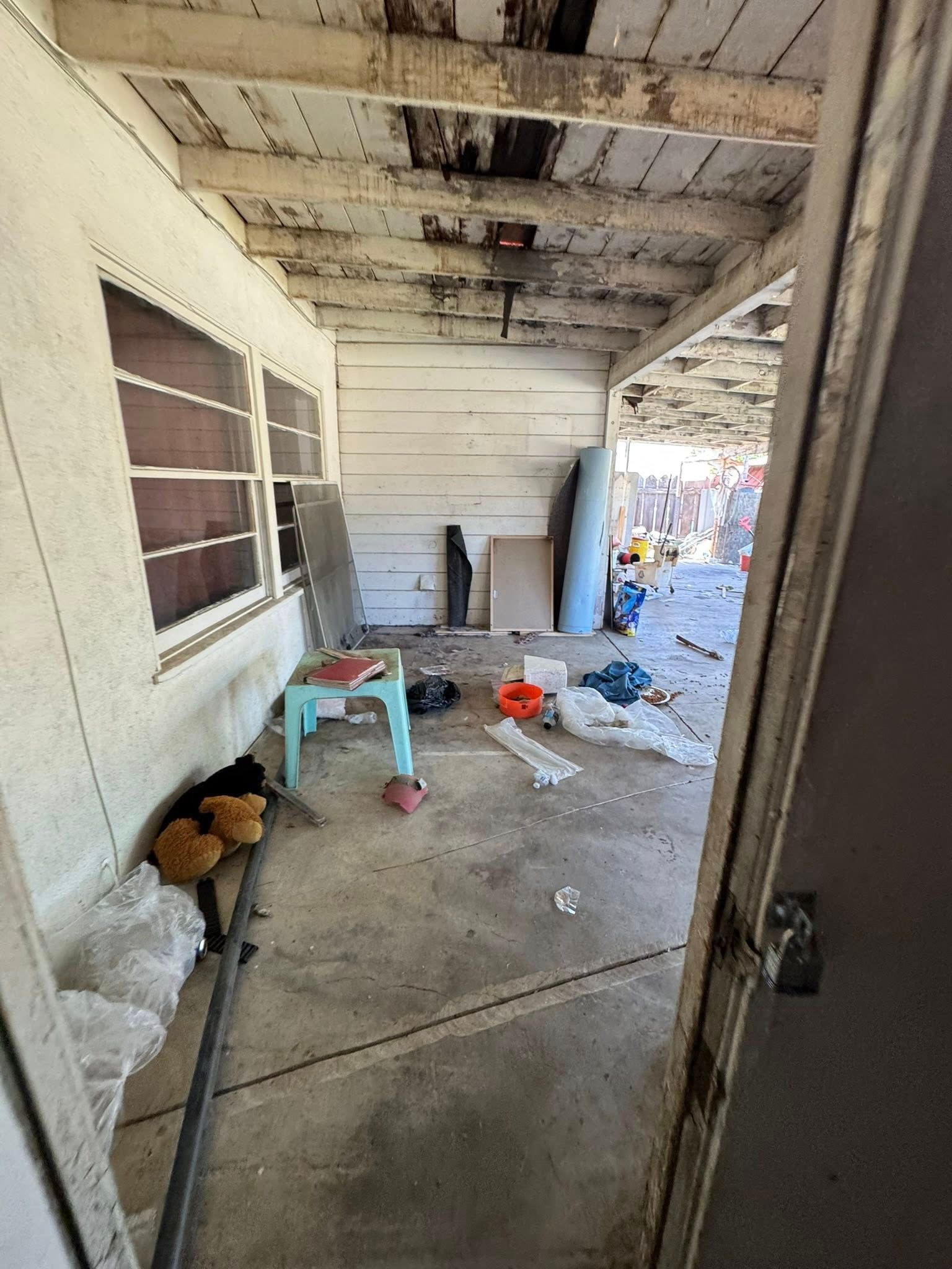 A cluttered porch with debris and damaged ceiling, viewed from a doorway.