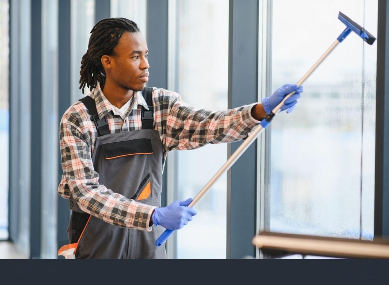 Person in overalls cleaning a window with a squeegee; indoors.