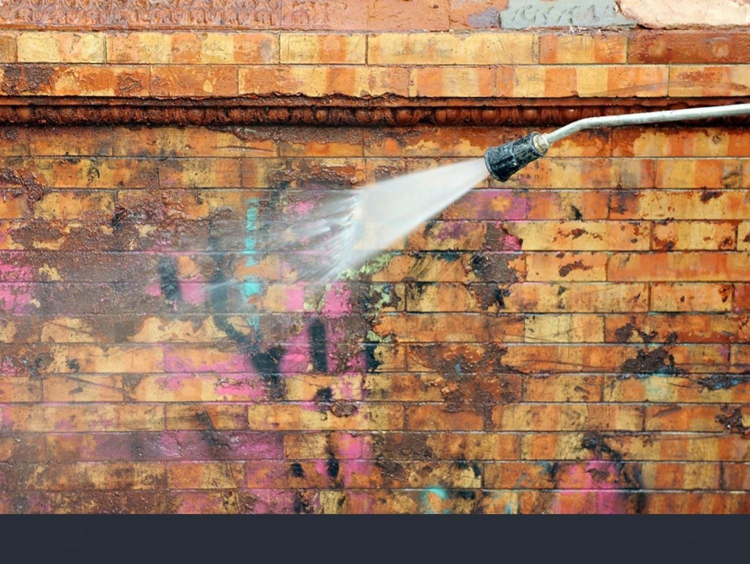 Pressure washer spraying a brick wall, removing colorful graffiti.