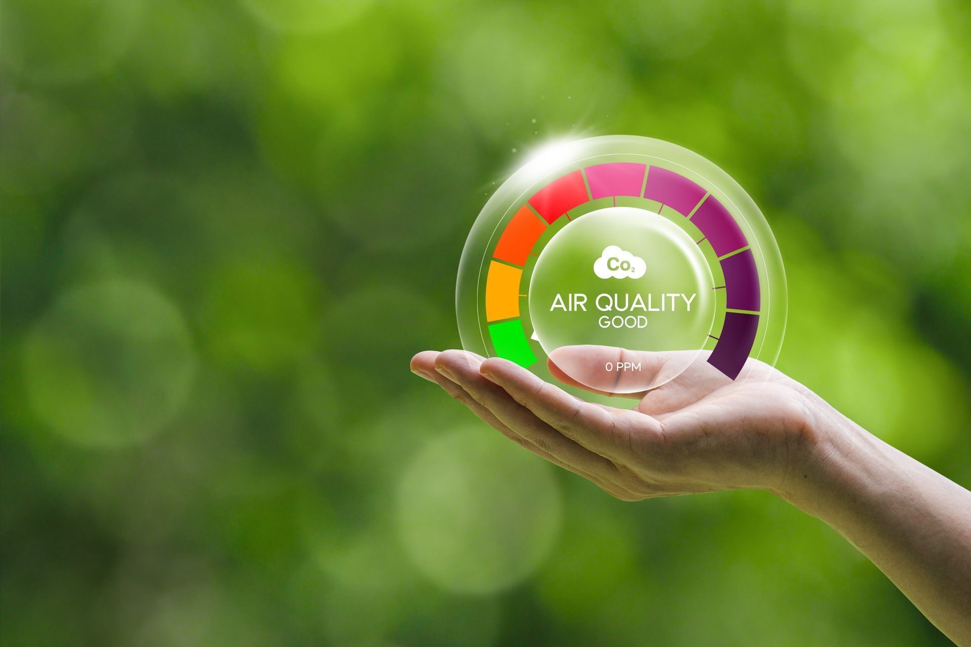 Hand holding a glowing air quality indicator with color-coded levels against a blurred green background.