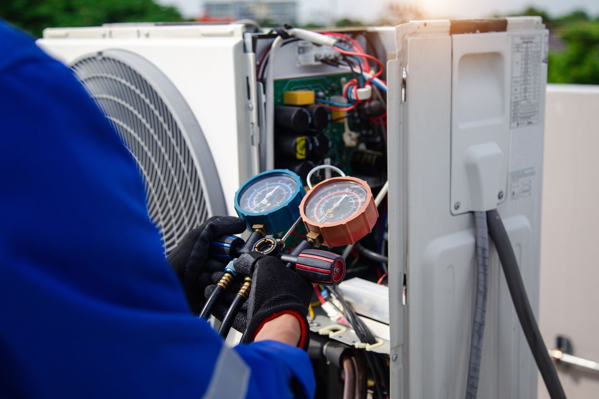 HVAC technician servicing an air conditioning unit outdoors, using gauges. Blue, red, black, white.