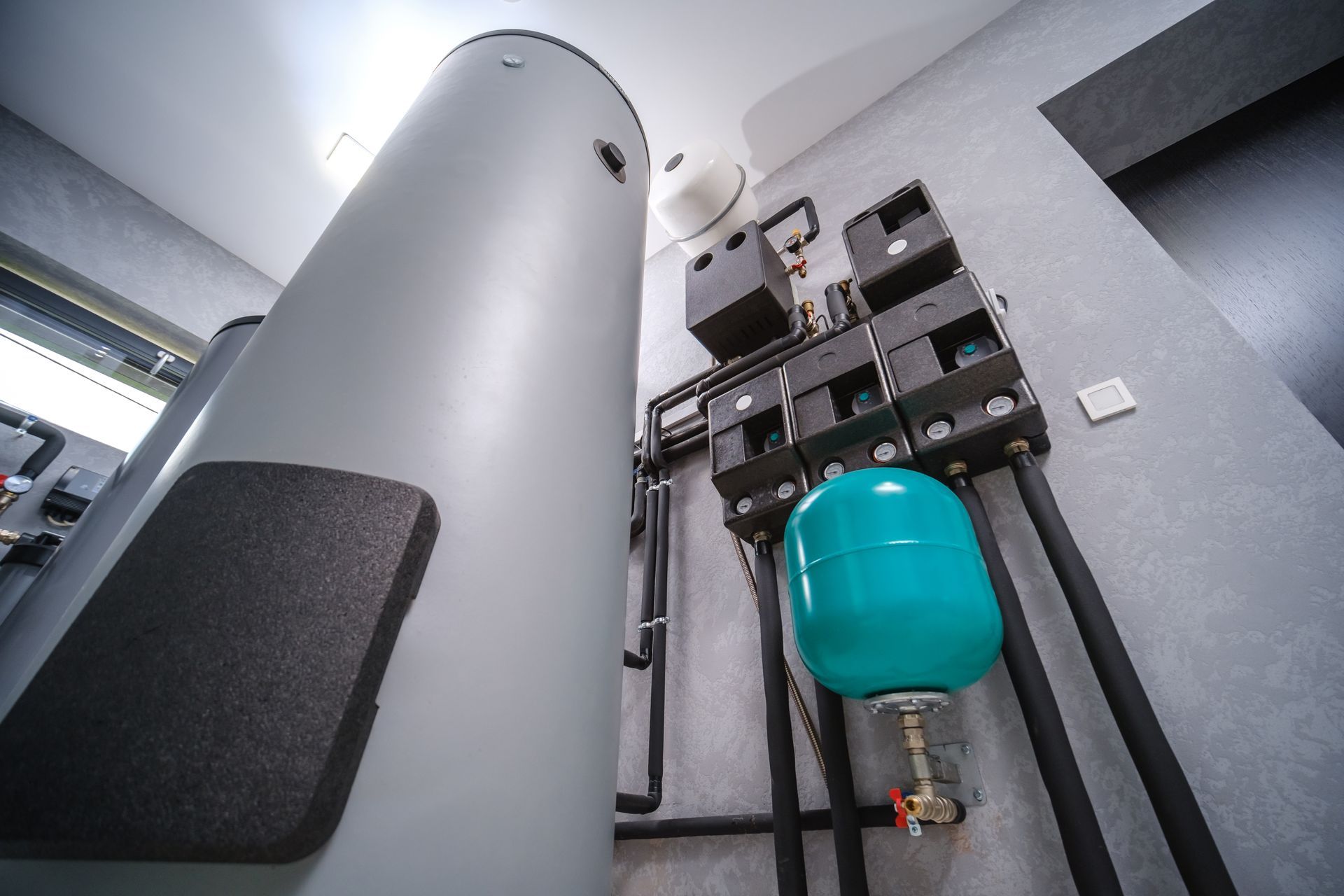 Large, gray water heater with plumbing, a blue pressure tank, and control panels in a utility room.