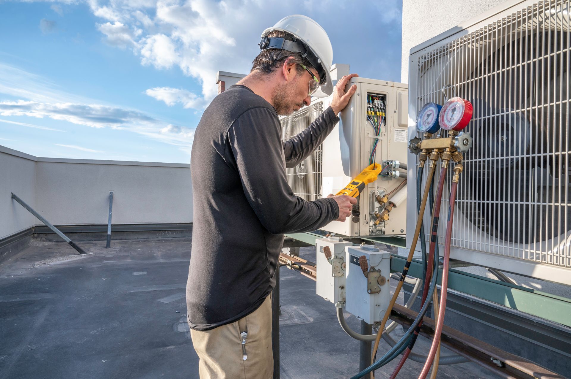 A man is working on an air conditioner on the roof of a building.