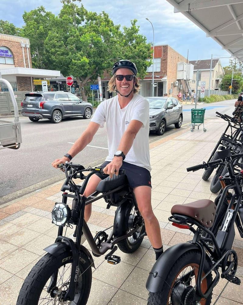 Man Smiles on Black Electric Bike in Front of Shops — E-Go-Try-Bikes in Nelson Bay, NSW