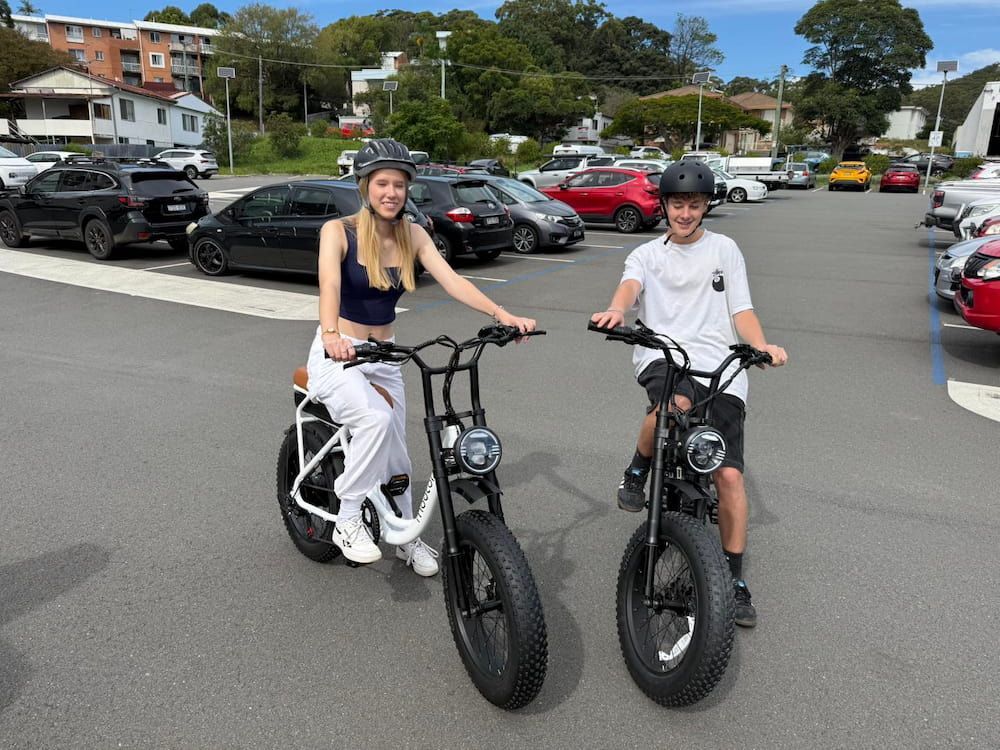 Two People on Electric Bikes in a Parking Lot, Smiling at the Camera — E-Go-Try-Bikes in Nelson Bay, NSW