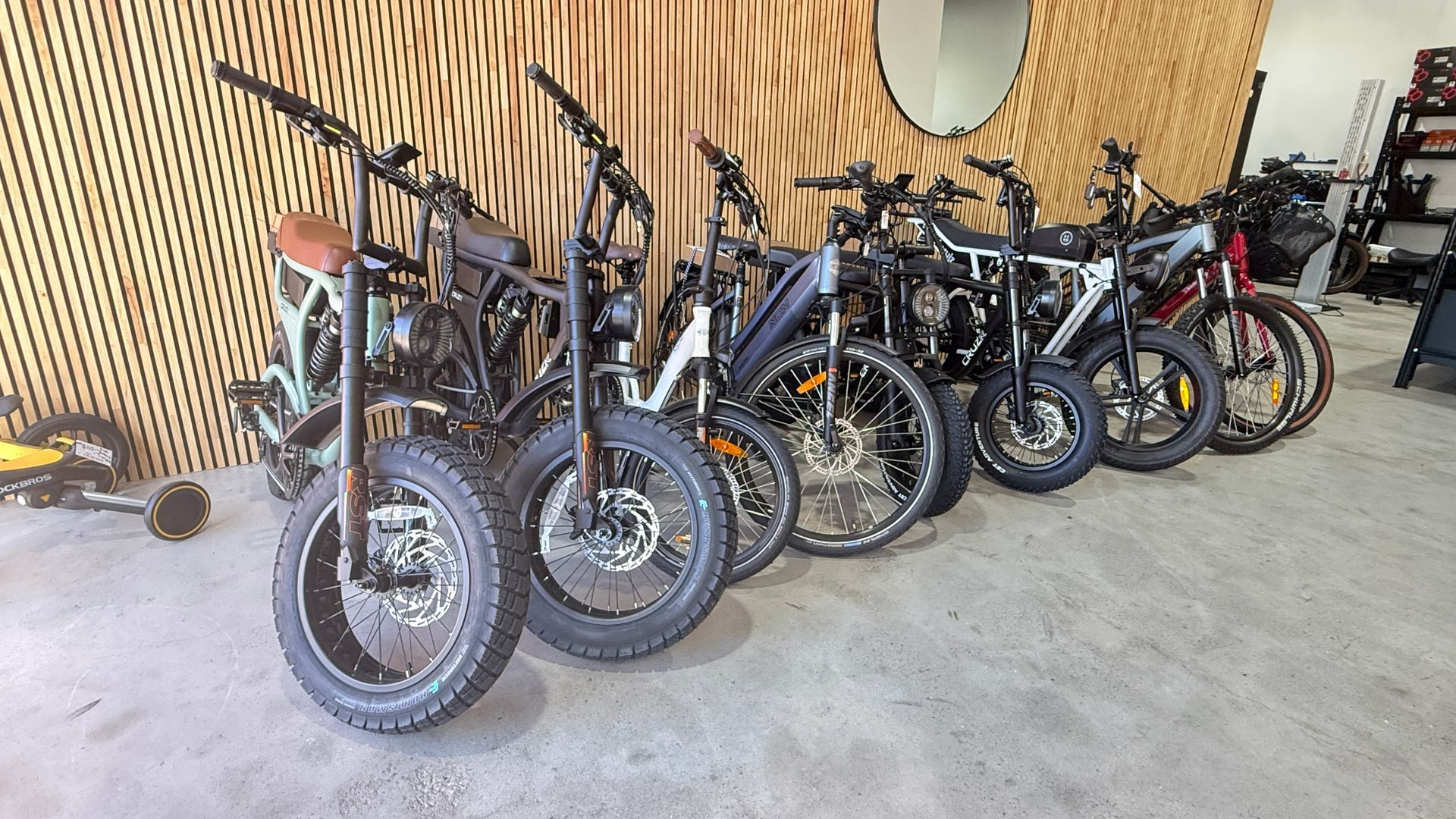 A row of several electric fat-tire bicycles parked in an indoor space with a decorative wood-slat wall.