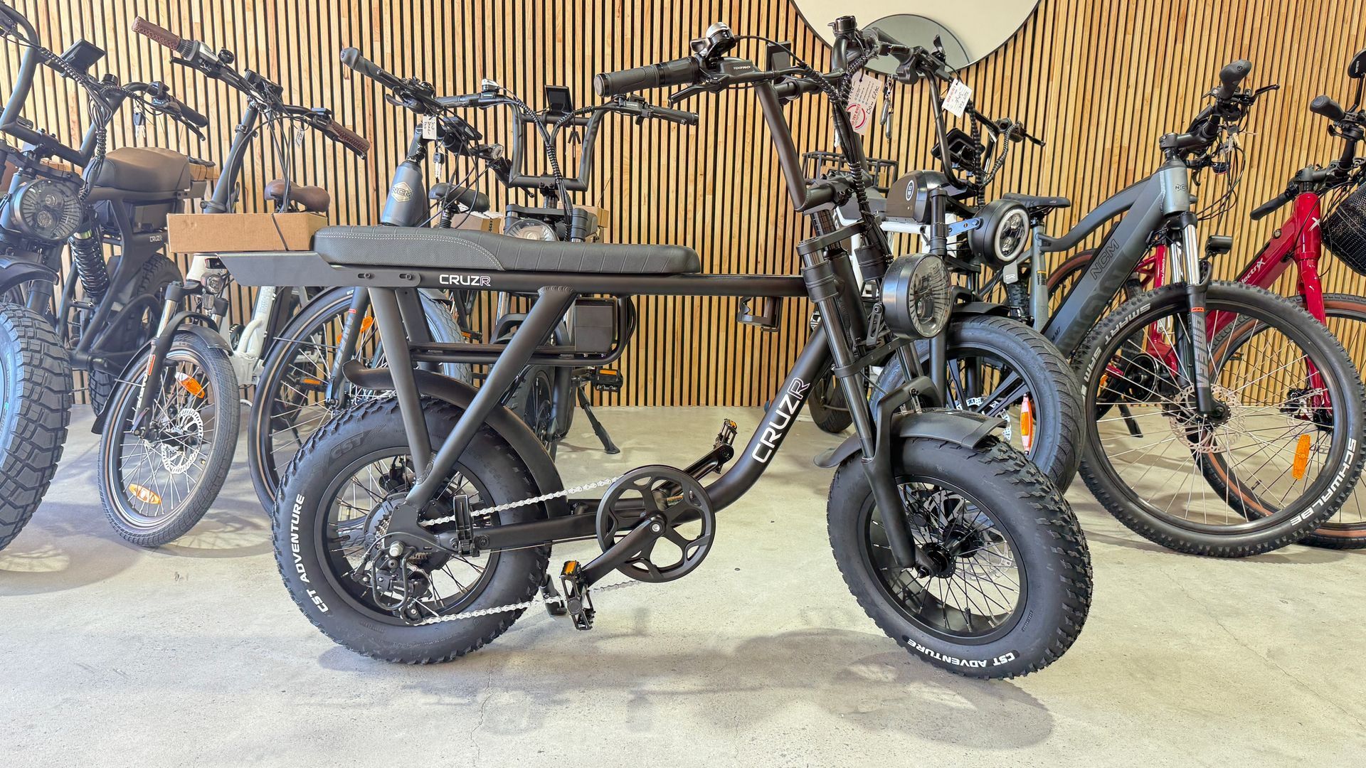 A row of electric bicycles lined up in a showroom, with a black moped-style e-bike in the foreground.