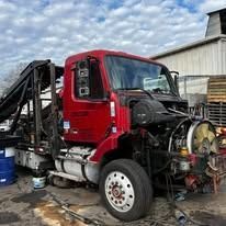 Red truck with hydraulic lift, various components exposed, outdoors.