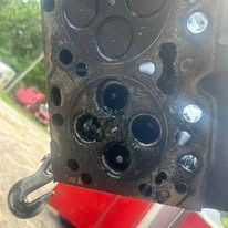 Close-up of a damaged engine cylinder head with various holes and markings.