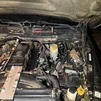 Engine bay of a vehicle with various components visible, including the engine block, fluid reservoirs, and wiring.