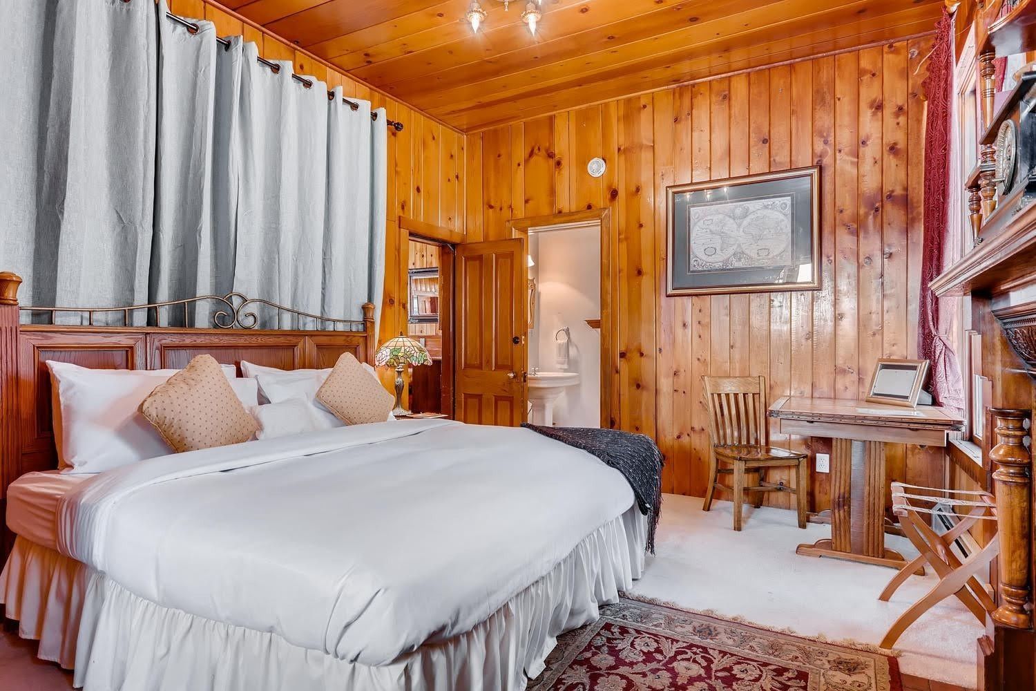 A bedroom with a king size bed , table , chairs and wood paneling.