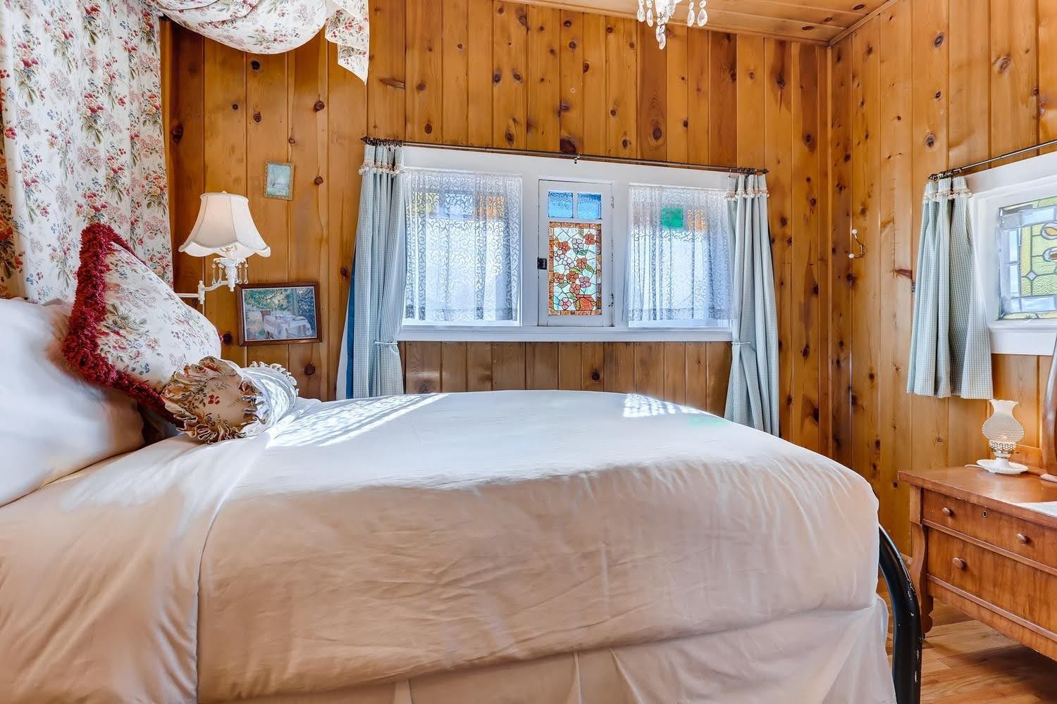A bedroom with wooden walls and a bed with white sheets.