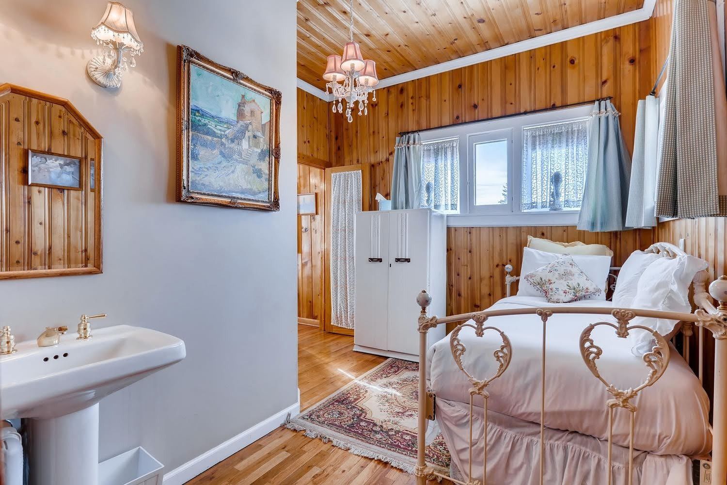 A bedroom with a bed , sink , mirror and painting on the wall.