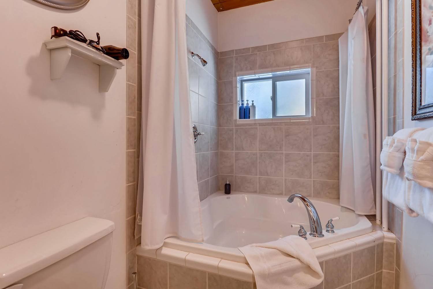 A bathroom with a tub , toilet , shower and window.
