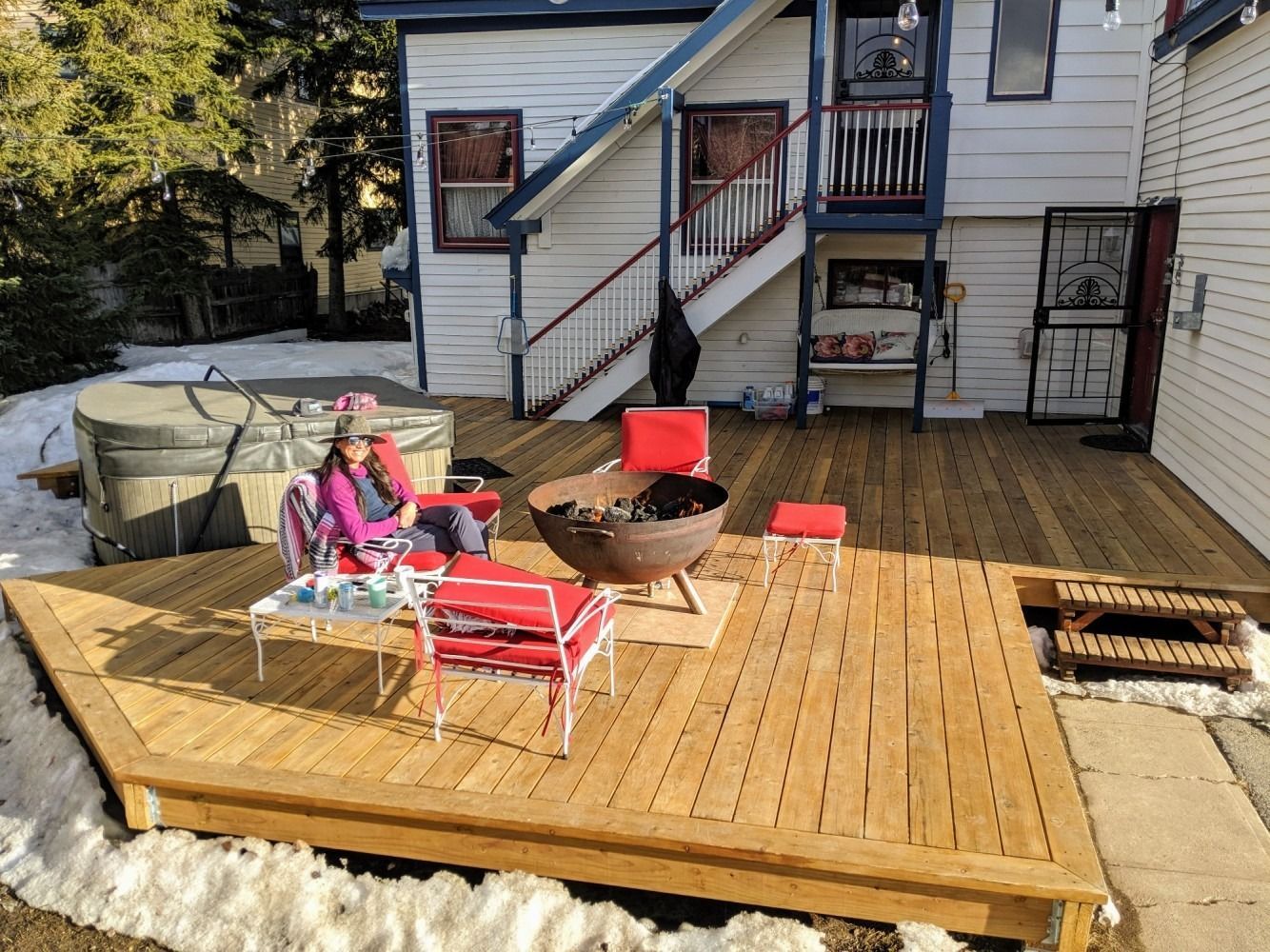 A woman is sitting on a wooden deck in front of a house.