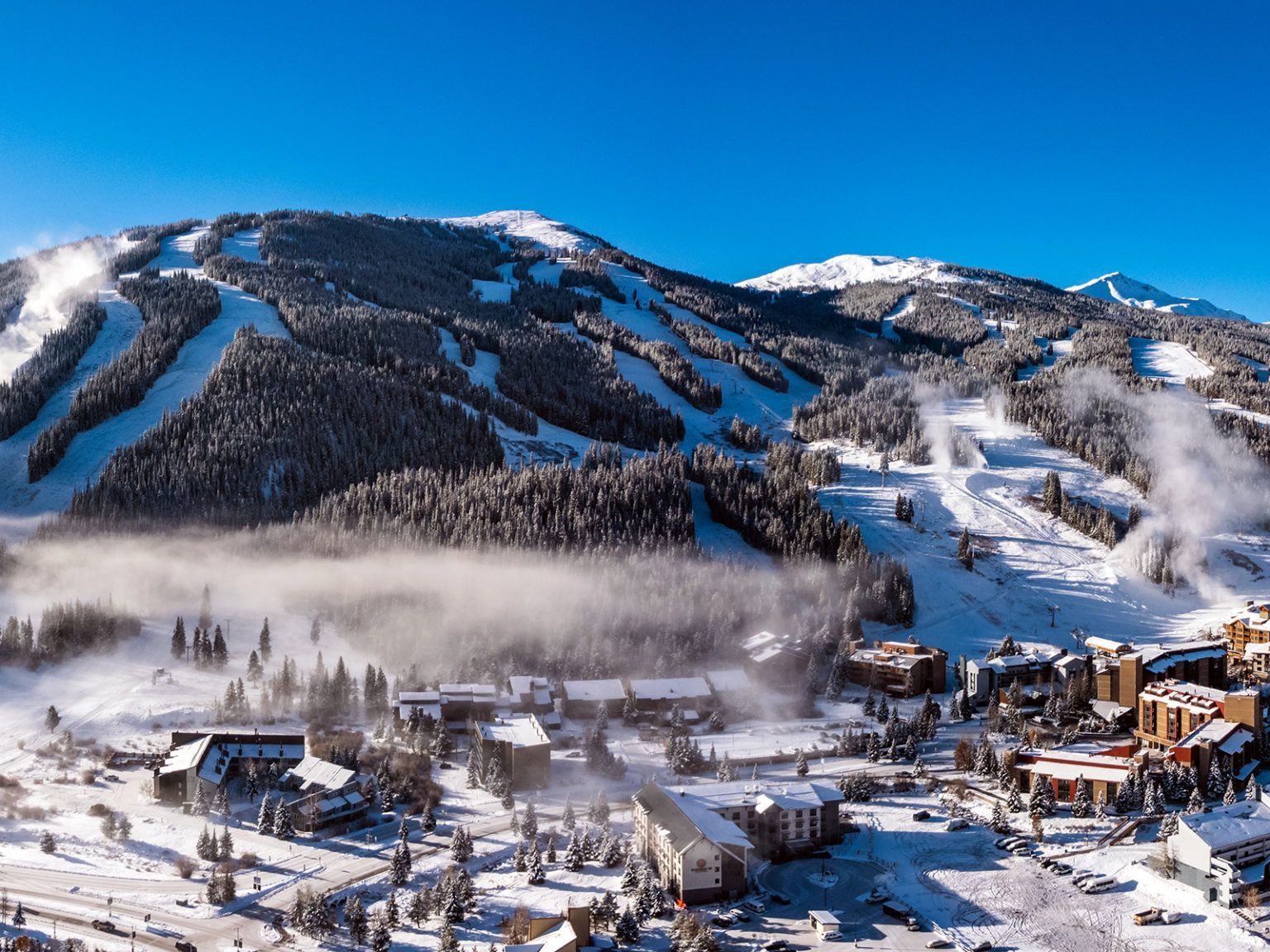 An aerial view of a snowy ski resort with mountains in the background.