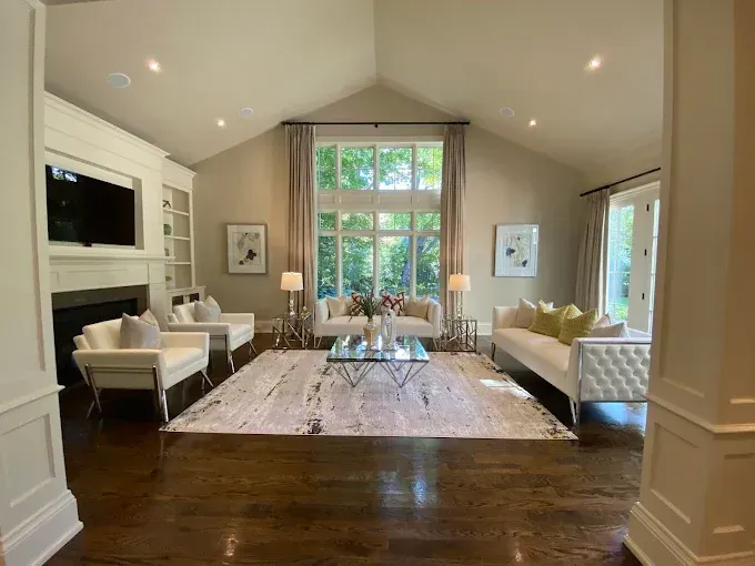 Elegant living room with white furniture, large window, and dark wood floors.