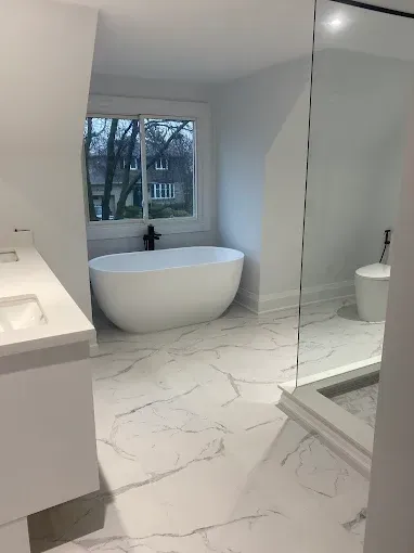 Bathroom with white marble-look tile, oval tub, and a large window overlooking trees.