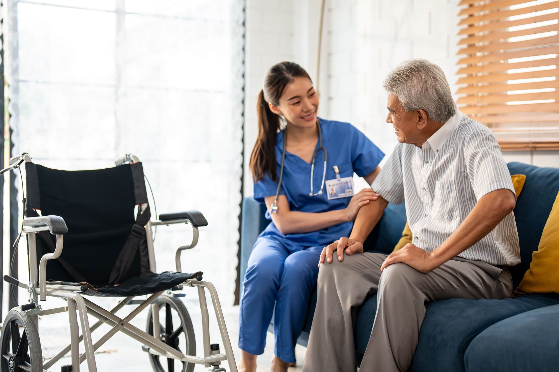 A nurse is sitting on a couch talking to an elderly man in a wheelchair.