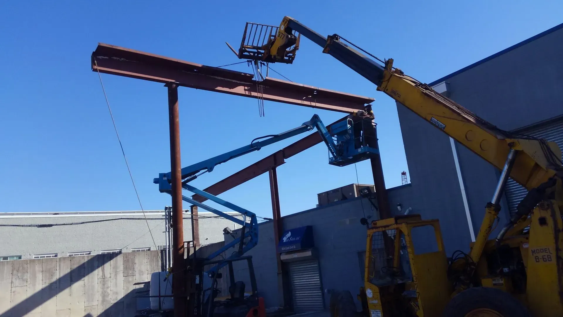 A forklift is lifting a large piece of metal in front of a building.