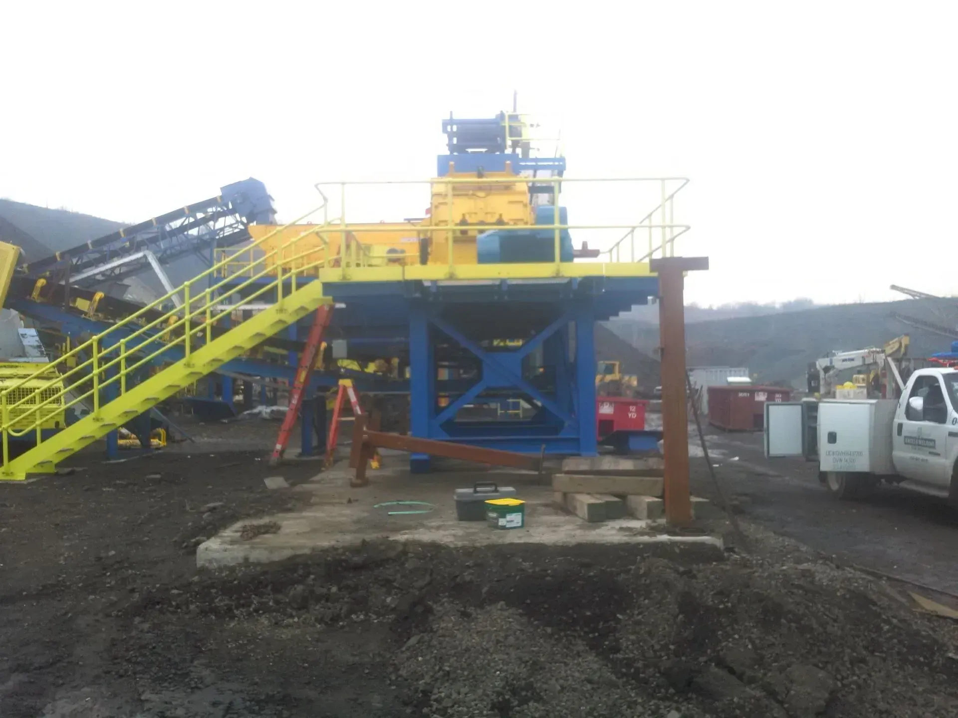 A truck is parked in front of a blue and yellow machine.