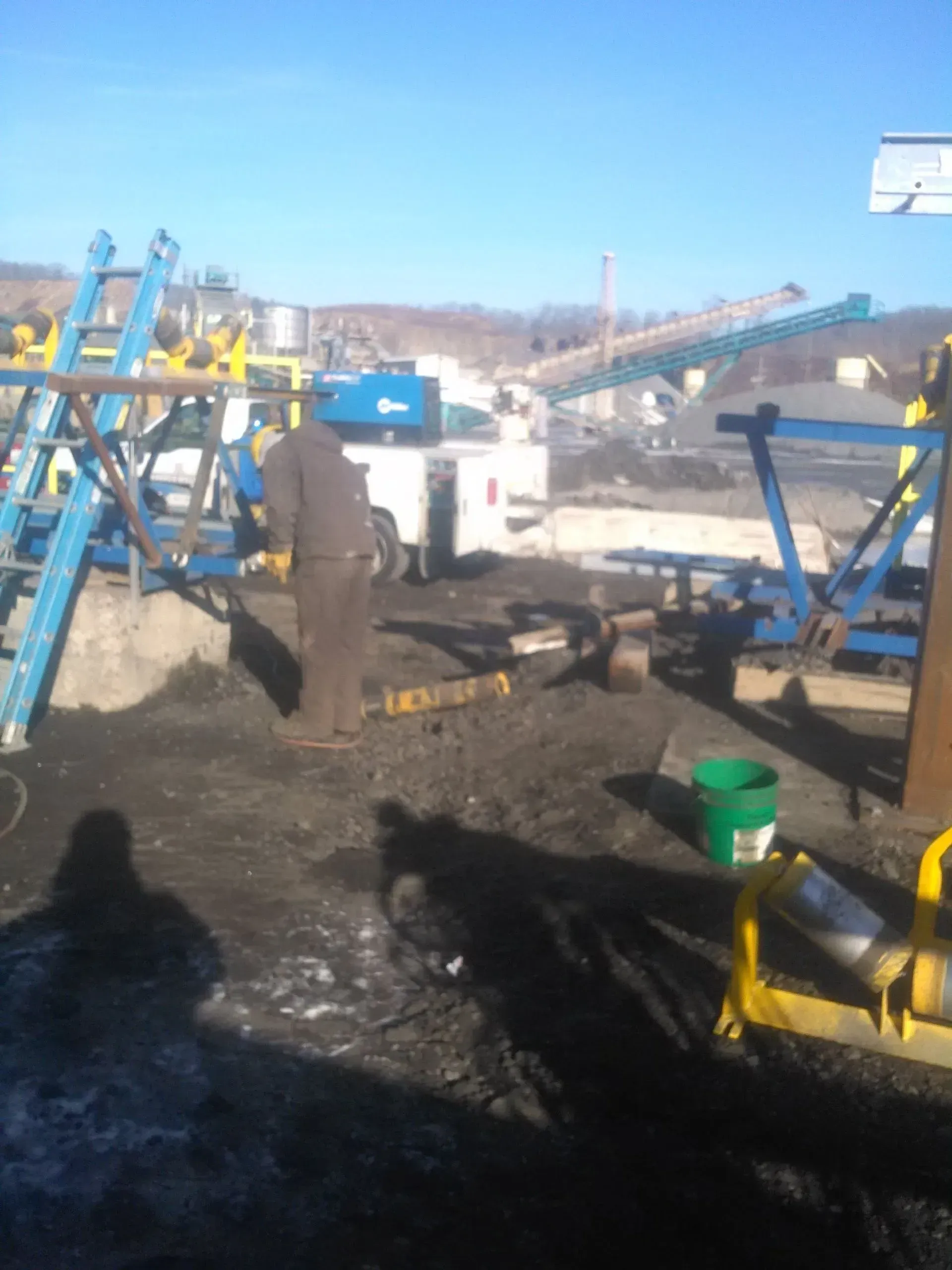 A man is standing in a field with a green bucket in front of him.