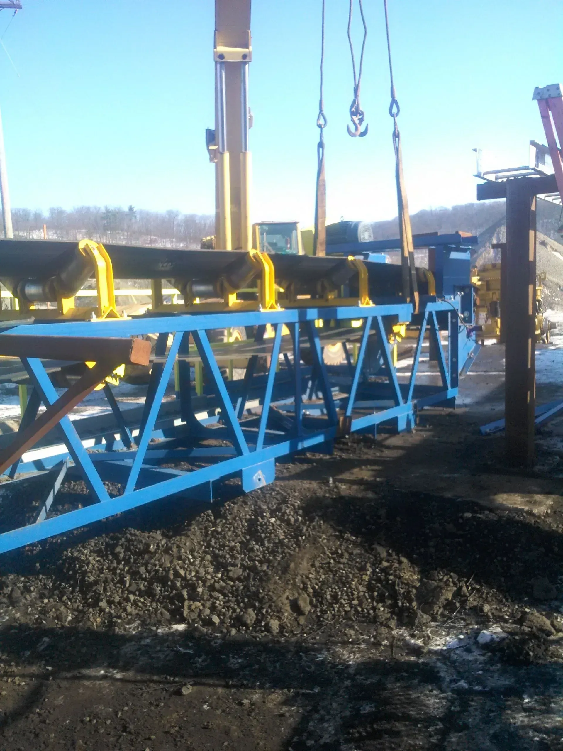 A blue and yellow conveyor belt is being lifted by a crane.
