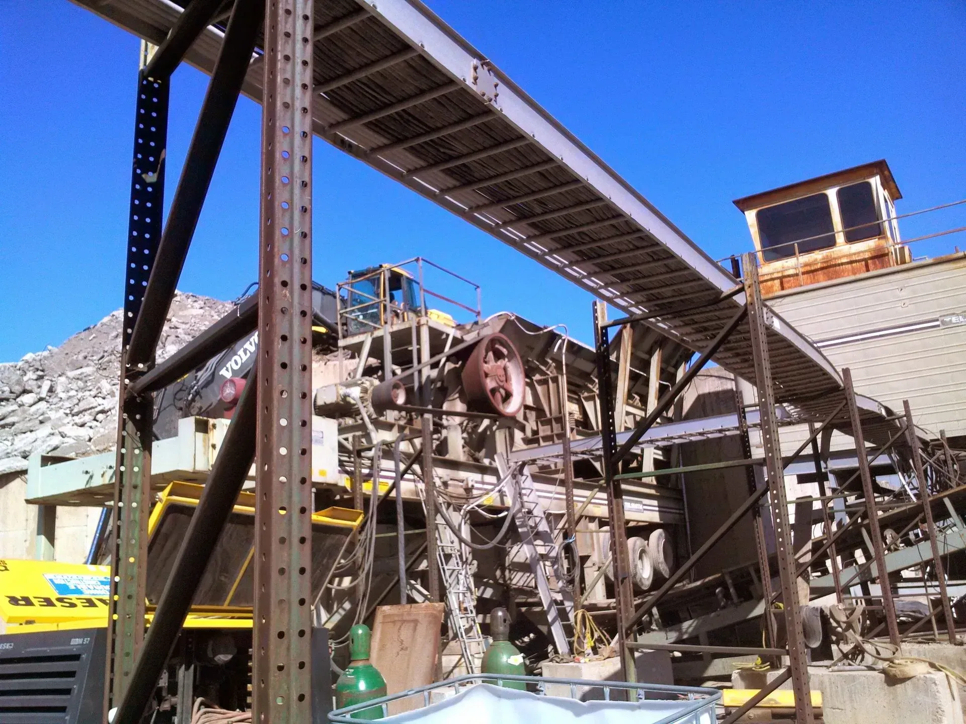 A yellow truck is parked next to a conveyor belt at a construction site.