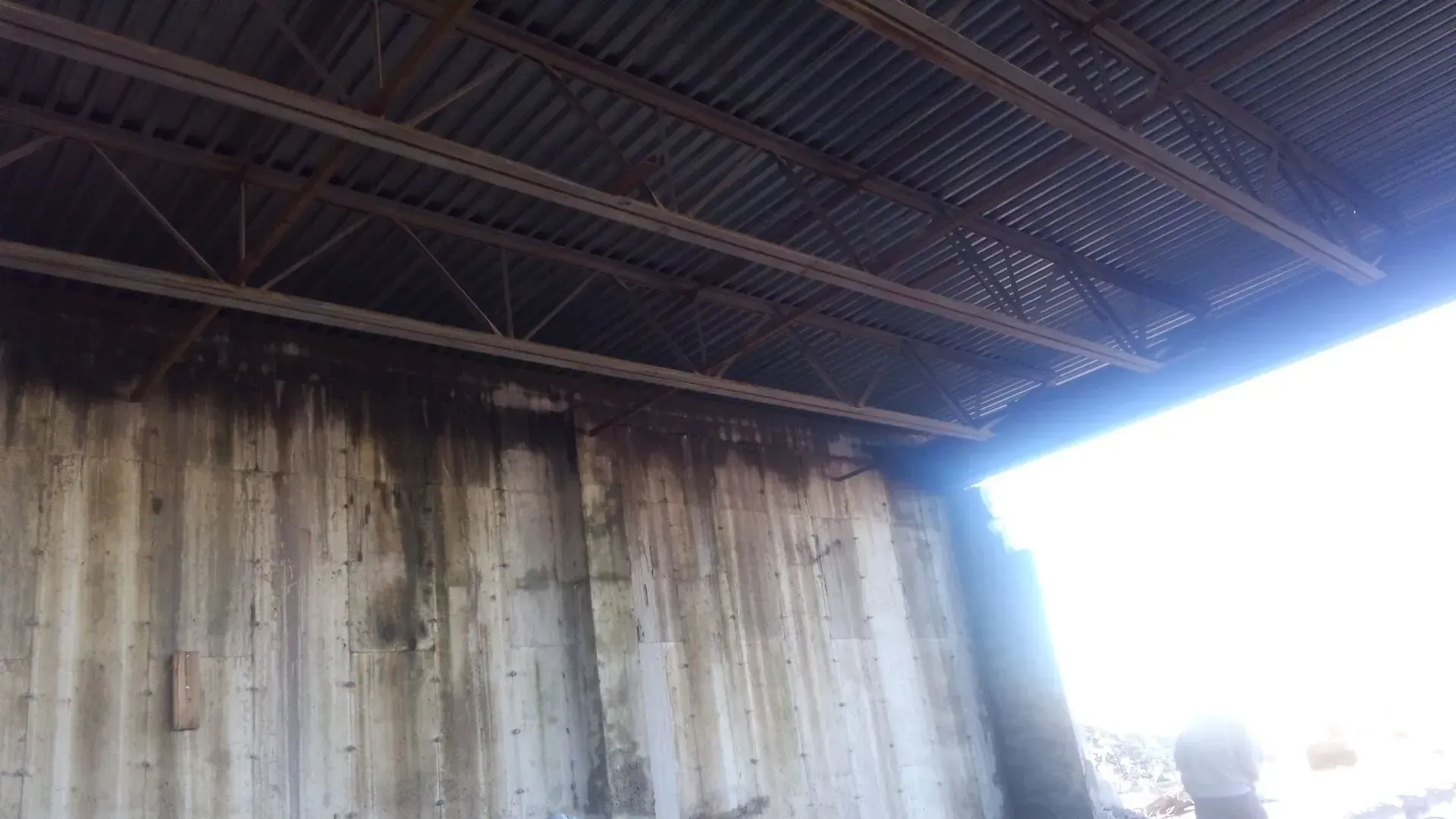 The inside of a building with a metal roof and a concrete wall.