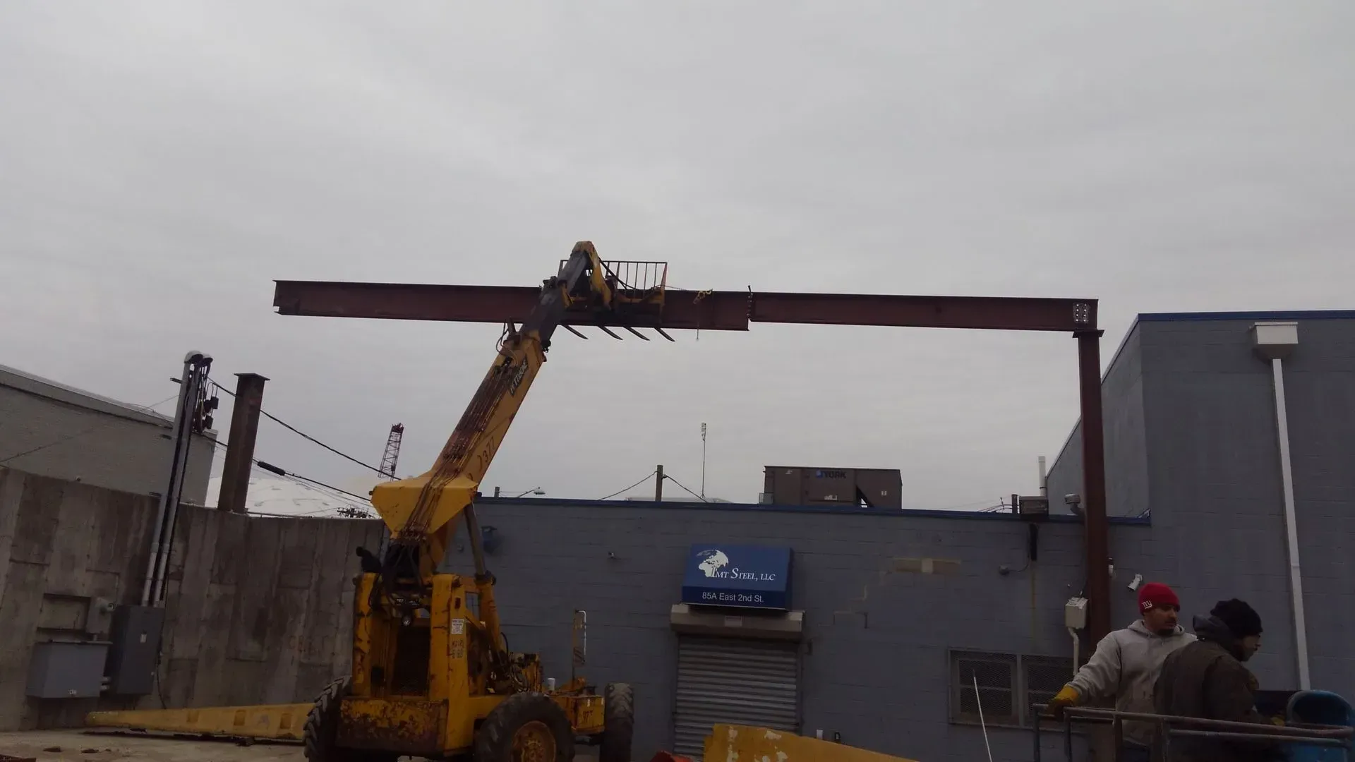 A crane is lifting a large piece of metal in front of a building.