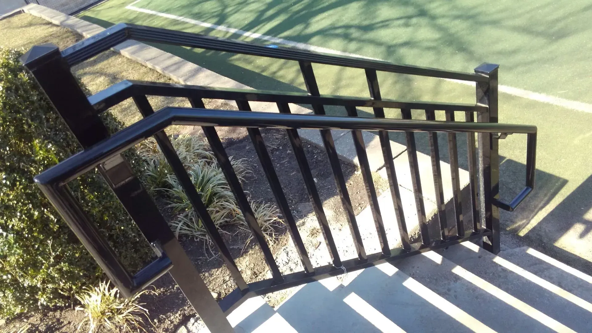 A staircase with a railing leading up to a tennis court.