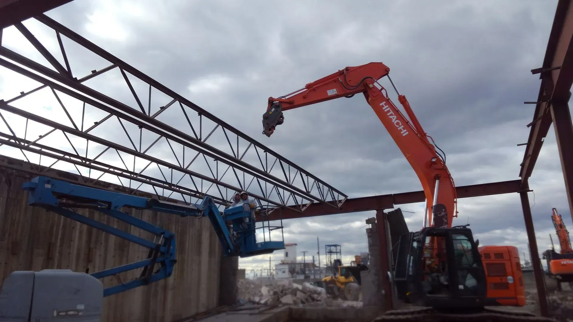 A large orange excavator is lifting a large metal structure.