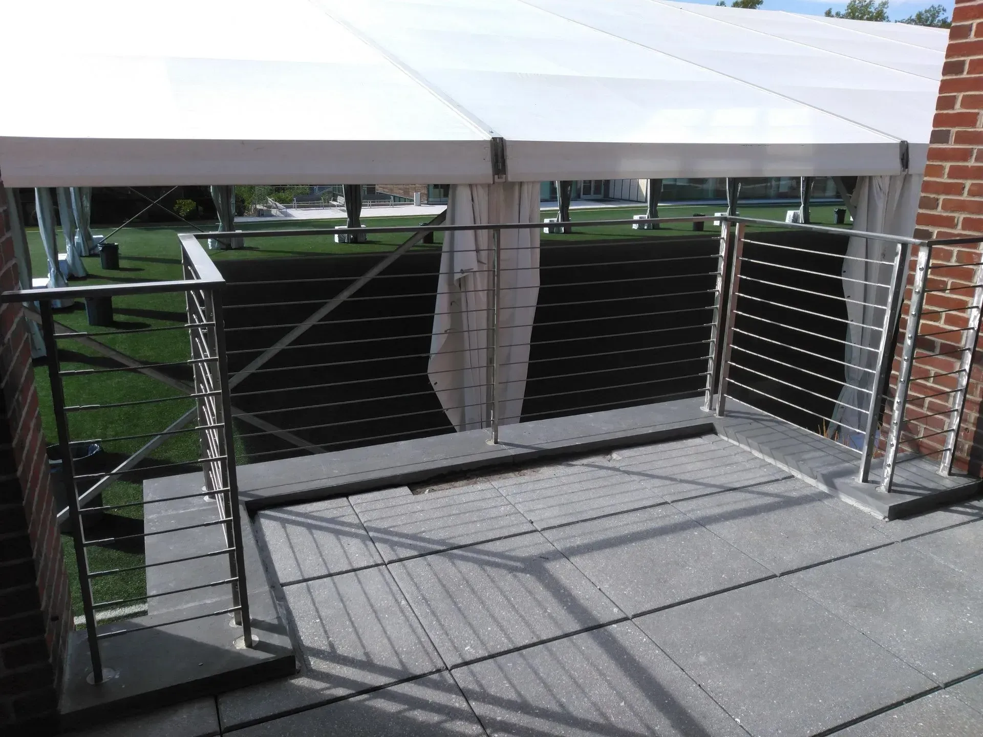 A balcony with a stainless steel railing and a white tent in the background.