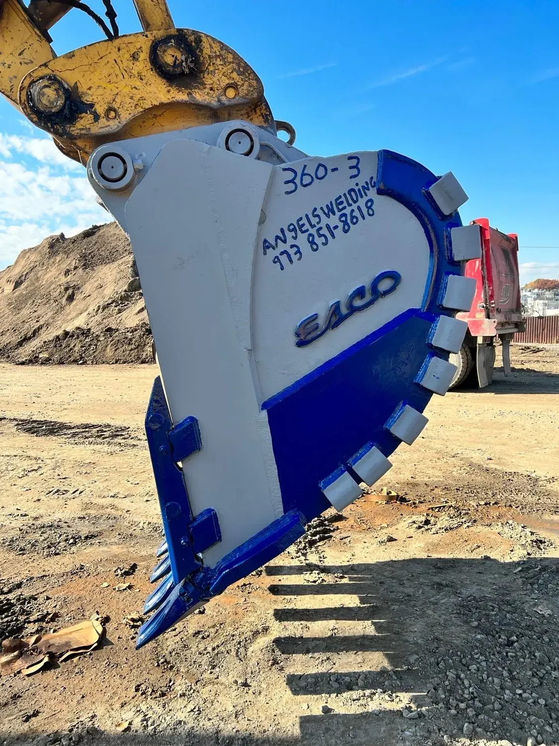 A blue and white excavator bucket is sitting on top of a dirt field.