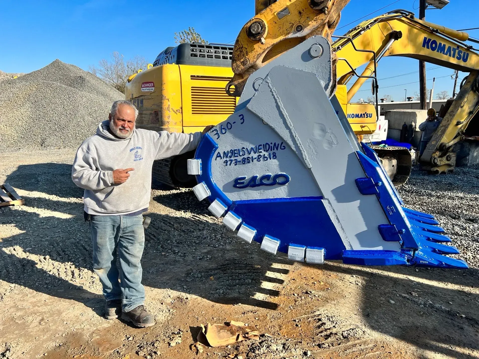 A man is standing in front of a large excavator bucket.