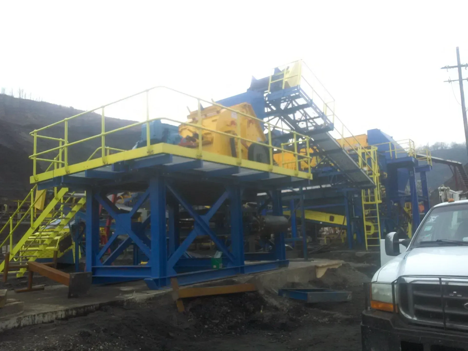 A white truck is parked in front of a large yellow and blue machine.