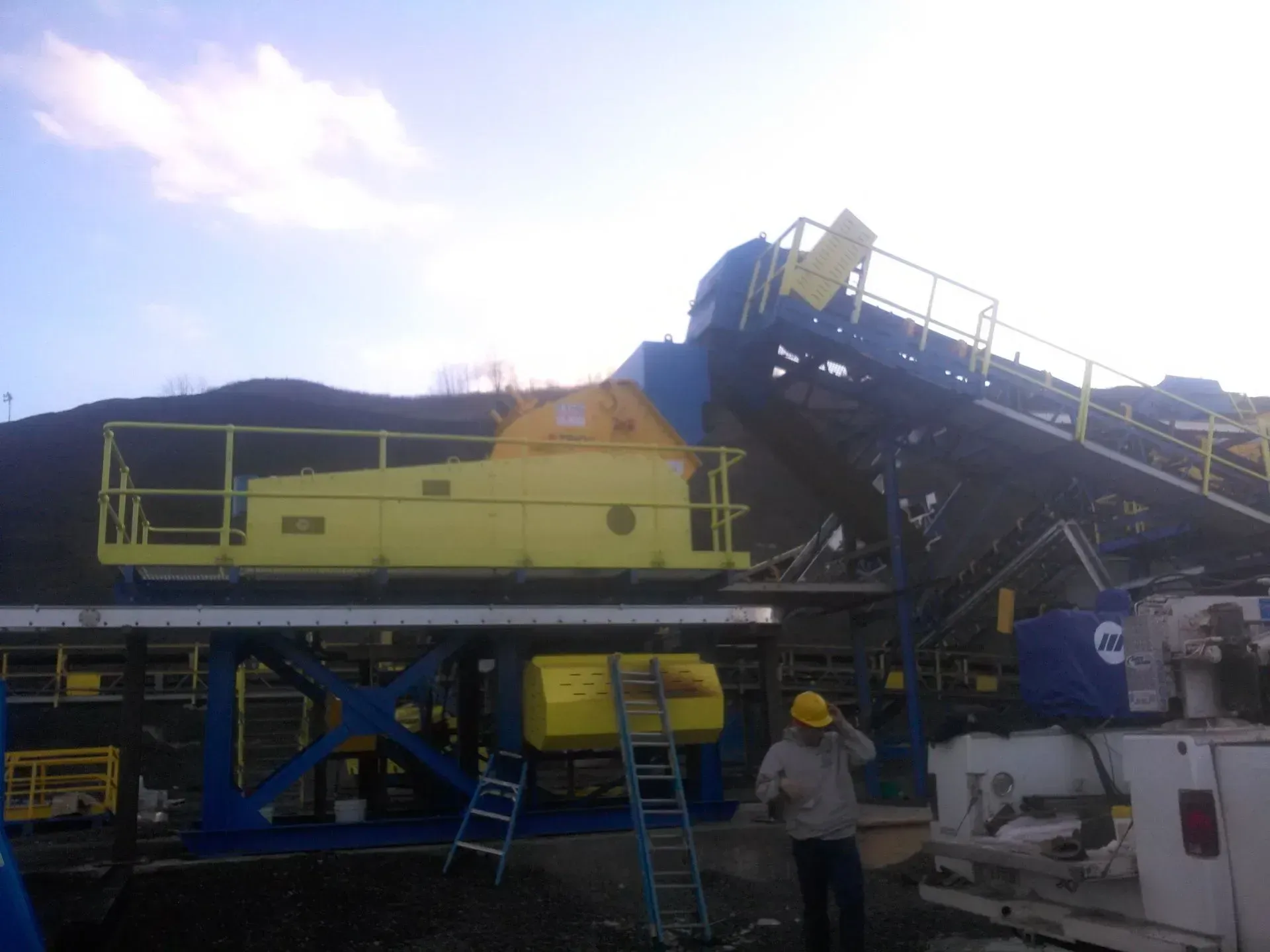 A man in a hard hat is standing in front of a large yellow and blue machine.