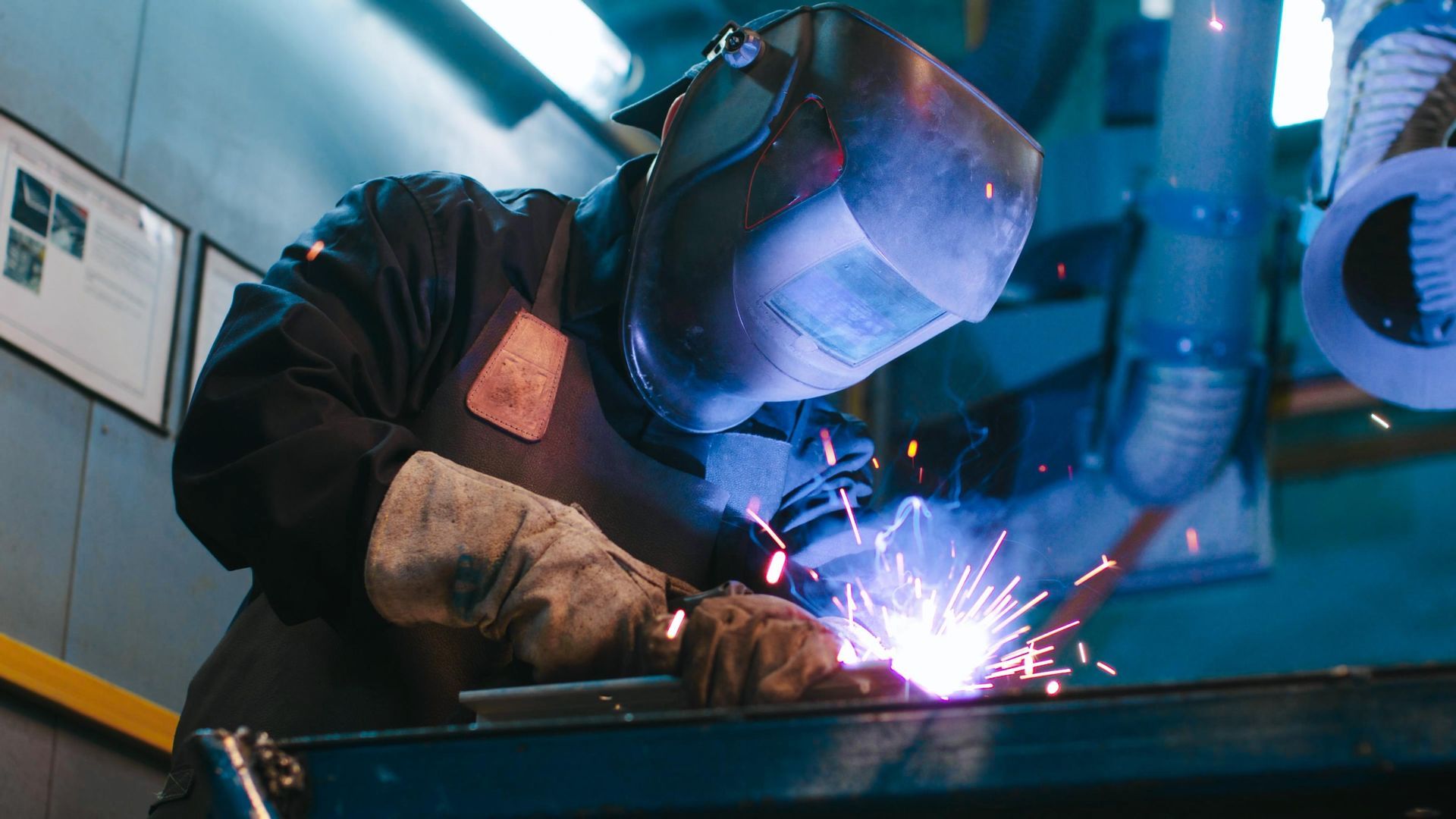 A man is welding a piece of metal in a factory.