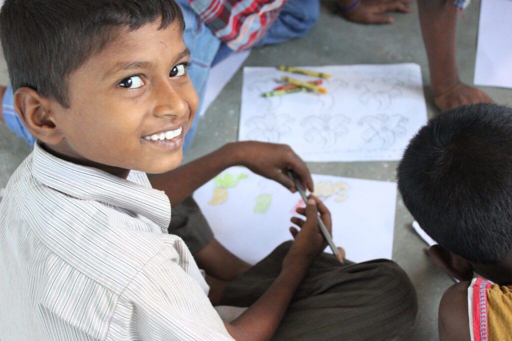 A young boy is sitting on the floor drawing with crayons.