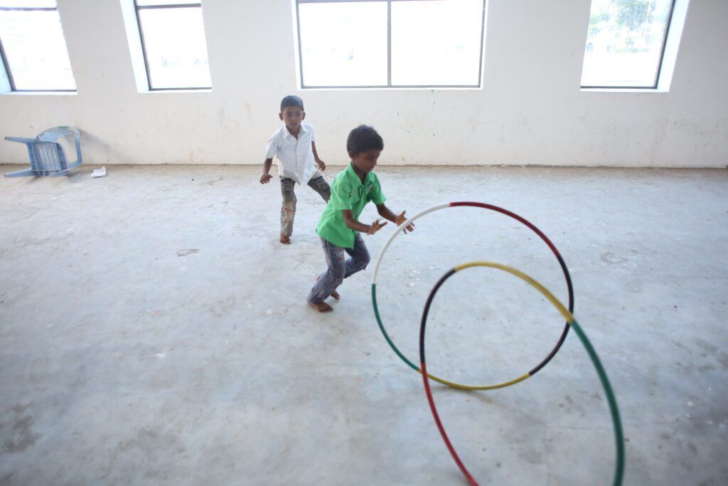 Two children are playing with hula hoops in an empty room