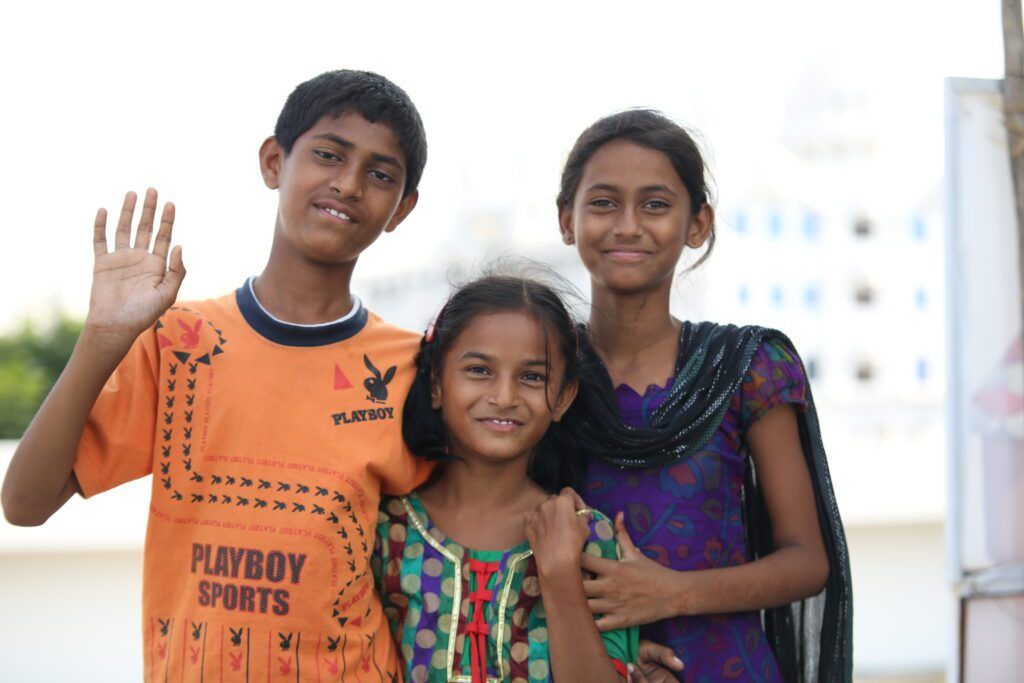 A boy and two girls are posing for a picture . the boy is wearing a playboy sports shirt.