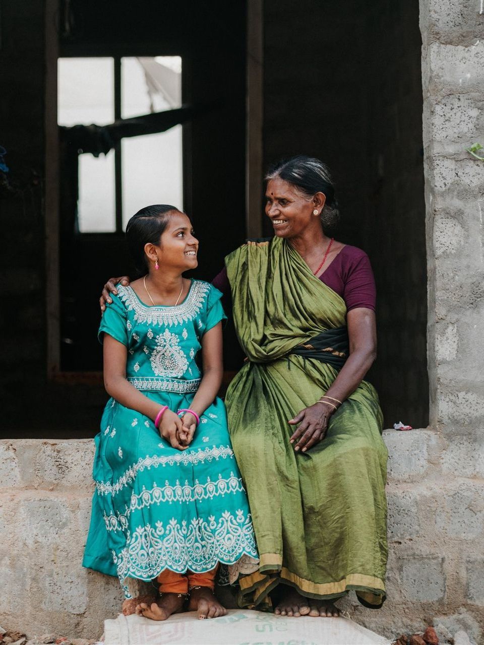 A woman in a green dress is sitting next to a little girl in a blue dress.