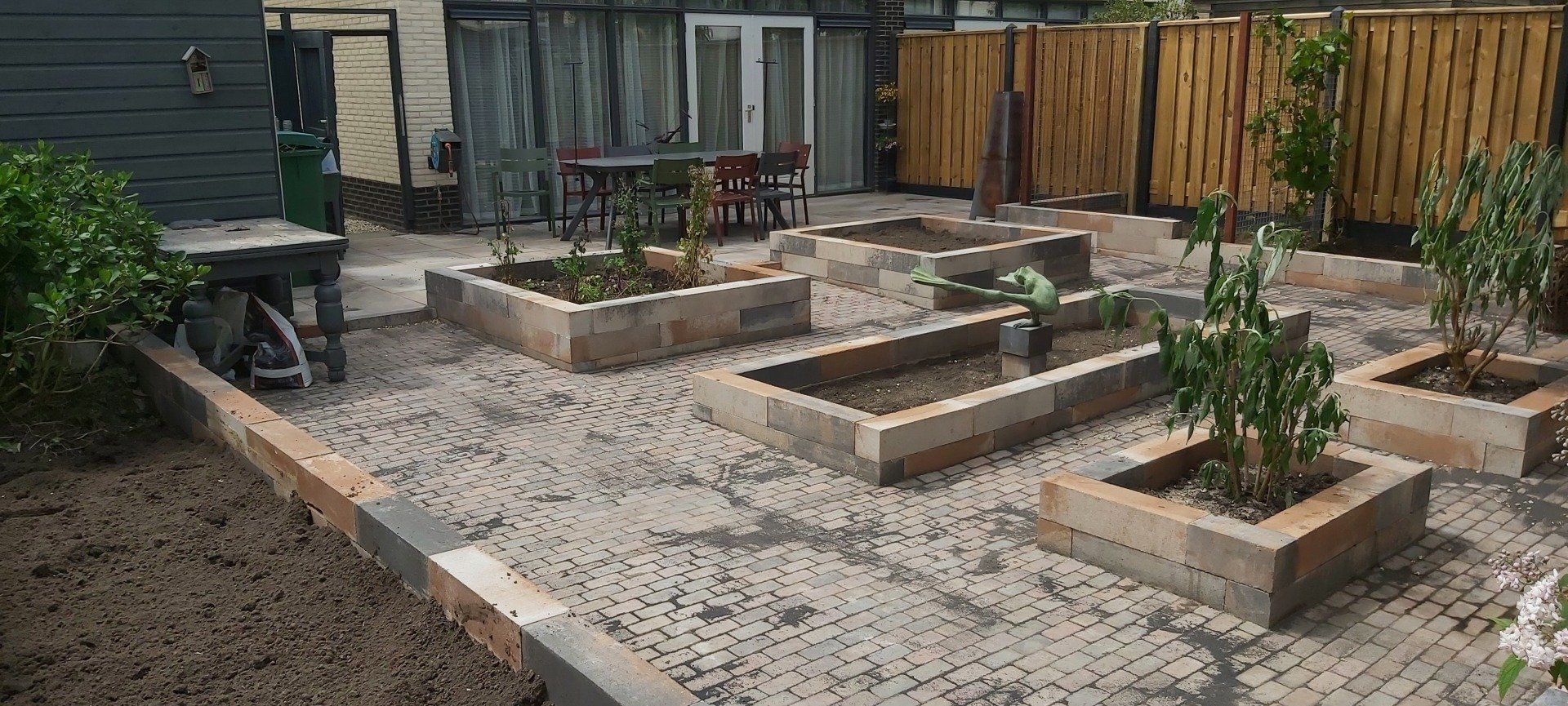 Een stenen tuin met een houten hek en een tafel en stoelen op de achtergrond.