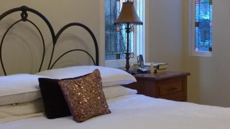 A bedroom with a bed , nightstand , lamp and stained glass window.