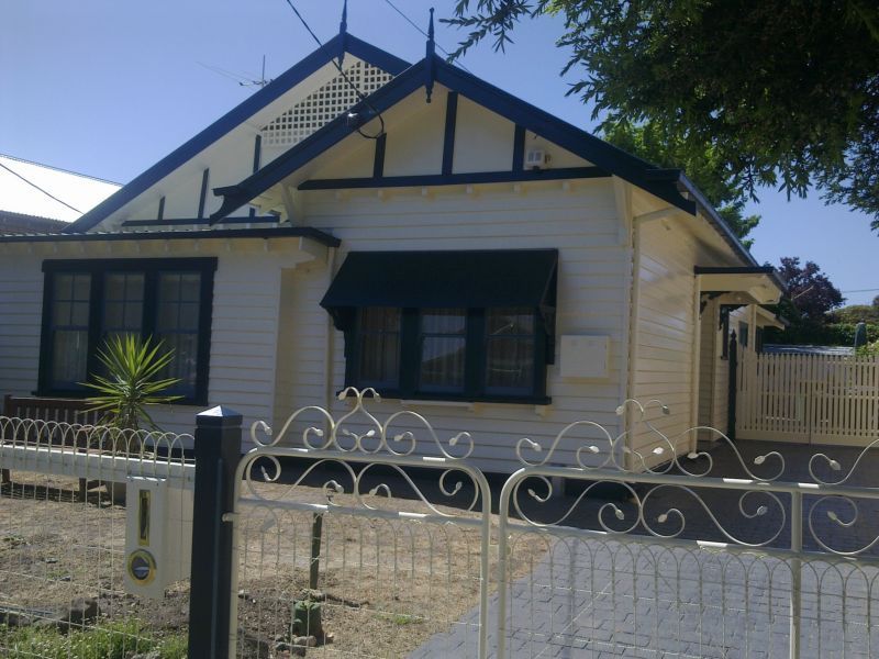A white house with a black roof is behind a wrought iron fence