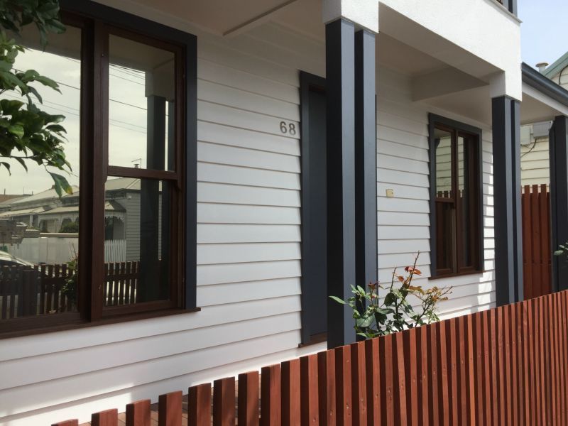 White house with brown-framed windows, dark gray pillars, and a red wooden fence. The house number 68 is visible.