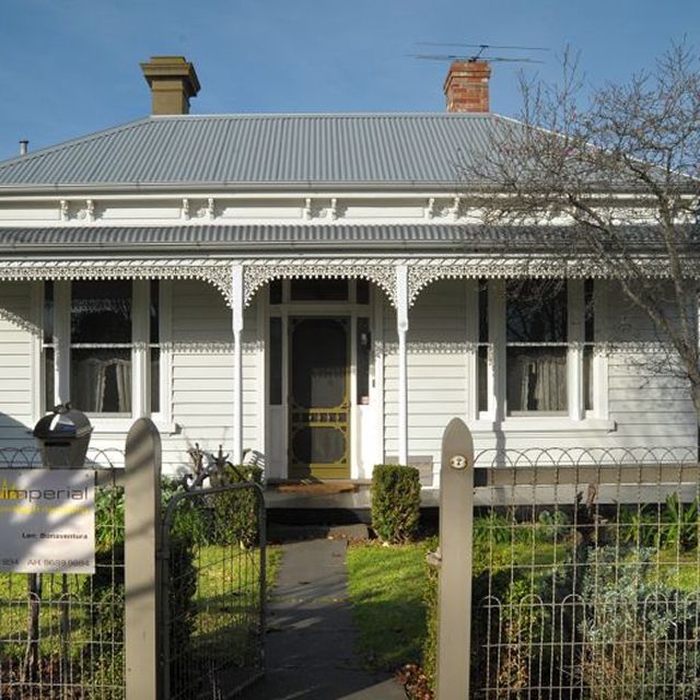 White Victorian-style house with decorative trim and a small front yard behind a fence.
